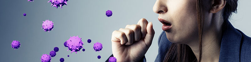 Person coughing, with hand over their mouth and large virus graphics being expelled from their cough. 